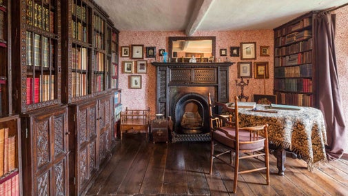 A view of the small library at Townend, with ornate wooden bookshelves on the left wall, a large fireplace on the back wall and a desk and chair to the right